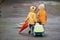 Two kids with umbrella, suitcase and yellow waterproof cloaks and boots walking outdoors after the rain together