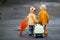 Two kids with umbrella, suitcase and yellow waterproof cloaks and boots walking outdoors after the rain together