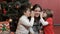 Two kids wisper into woman`s ears near the christmas tree