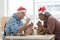 Two kind senior carpenter men Caucasian and asian wearing santa hat painting color with brushes on wooden toy house at workshop