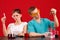 Two laboratory assistant are studying some kind of liquid in flasks. On a red background.