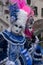 Two ladies holding fans, and wearing hand painted masks and ornate blue and pink costumes at Venice Carnival.