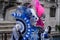 Two ladies holding fans and wearing hand painted masks and ornate blue and pink costumes at Venice Carnival