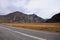 A two-lane asphalt road with fences, leading directly through a picturesque autumn valley at the foot of high mountains