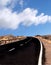 Two lane empty road curving to the horizon in a rugged desert landscape with blue cloudy sky