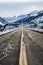 Two lane paved road ascending into snowy mountains