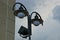 Two lanterns on a black pillar against the sky and clouds at the gray wall