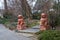 Two large exotic marble red dog statues surrounded by lush green trees near a long winding footpath in the garden