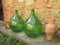 Two large green oil or wine bottles and a terra-cotta amphora against a brickwork in Tuscany, Italy.