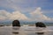 TWO LARGE ROCK ADORN THE BEACH WITH A CLOUDY BLUE SKY CREATING  A C HARMING ATMOSPHERE