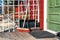 Two large stiff hard PVC yard brushes for Outdoor sweeping red and brown stand close to green entry door and small black doormat