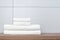 Two large and two small neatly folded white towels lie on a wooden shelf against the background of ceramic tiles