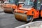 Two large vibratory road rollers compact the fresh asphalt on a new stretch of road