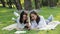 Two laughing smiling pretty girls lying on grass in city park, discussing selfie on smartphone. Couple of beautiful
