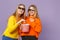 Two laughing young blonde twins sisters girls in 3d imax glasses watching movie film, hold popcorn  on pastel