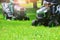 Two lawn mowers trimming green grass on a meadow