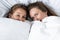 two lesbians lying under white blanket in bedroom.