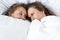 two lesbians lying under white blanket and looking at each other in bedroom.