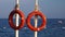 Two lifebuoys hang on a pole in the sea, people are bathing