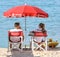 Two lifeguards under a red parasol on the beach, Cannes.