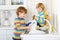 Two little blond kid boys washing dishes in domestic kitchen