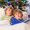 Two little blond sibling boys reading a book on Christmas