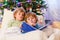 Two little blond sibling boys reading a book on Christmas