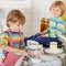 Two little blond twins boys washing dishes in domestic kitchen