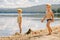 Two little boys in caps stand on the sandy shore of the lake