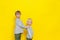 Two little boys in a great mood. The older brother holds his brother by the shoulders. Yellow colored background.