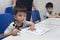 Two little boys learning to write with a pencil in classroom at school