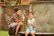 Two little boys sit on a wooden bench by the ancient wall and eat bananas with appetite