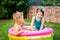 Two little brother and sister playing and splashing in pool on hot summer day. Children swimming in kid pool. Two cheerful cute