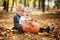 Two little brothers sitting on grass and embracing with huge pumpkin in autumn day .