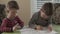 Two little brothers are sitting at the table and draw together on the same coloring. The older brother teaches thhappy