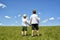 Two little brothers stand holding hands on a green field against a blue sky and clouds. Brotherhood and friendship