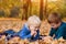 Two little brothers using smartphone, lying in yellow autumn leaves. Smiling and having fun. Fall day