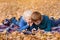 Two little brothers using smartphone, lying in yellow autumn leaves. Smiling and having fun. Fall day