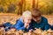 Two little brothers using smartphone, lying in yellow autumn leaves. Smiling and having fun. Fall day