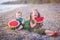 Two little children, boy girl, eating watermelon on the beach, summertime enjoying beautiful day close to ocean