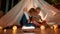 Two little children, brother and sister reading a book together while sitting on a blanket in a teepee made with