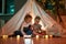 Two little children, brother and sister reading stories together while sitting on a blanket in a teepee made with