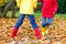 Two little children playing in red and yellow rubber boots in autumn park in colorful rain coats and clothes. Closeup of