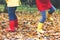 Two little children playing in red and yellow rubber boots in autumn park in colorful rain coats and clothes. Closeup of