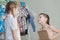 Two little children standing near a hanger with clothes at home