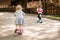 Two little cute girls ride their scooters in the park.