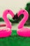 Two little flamingos kiss on the green grass in front of the pool. Flamingos in the form of a heart. Coasters for the pool. The