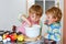 Two little funny brothers baking apple cake in domestic kitchen. Happy healthy kid boys having fun with working with