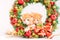 Two little funny red kittens peek out of the Christmas wreath on bright background