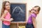 Two little girls draw with chalk on blackboard